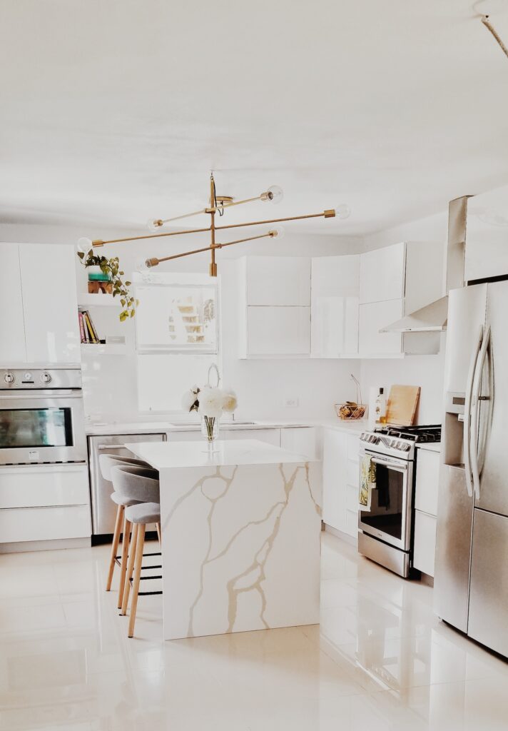 Modern kitchen interior with white cabinets and island, featuring a stylish gold light fixture overhead. Search for 'kitchen remodelers near me' to achieve this look.