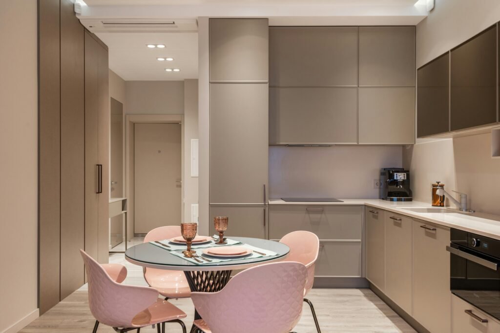 Modern home renovation cost-efficient design in NYC showcasing neutral-toned cabinets, a sleek coffee machine, and a dining area with pink chairs