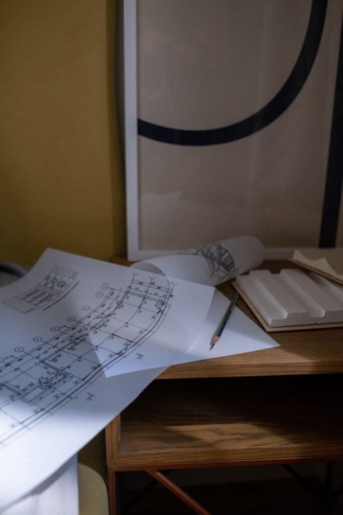 Architectural blueprints and sketches on a wooden table with a framed artwork in the background, showcasing house remodel planning.