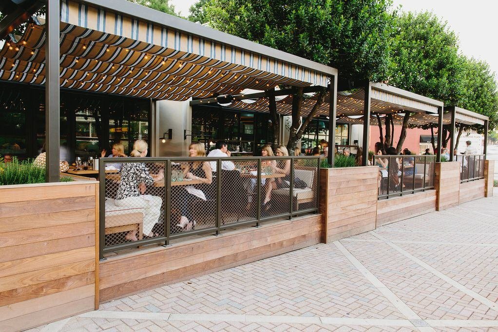 Outdoor dining Shed space with wooden barriers and structured seating under a striped awning, set on a paved area adhering to urban restaurant regulations.